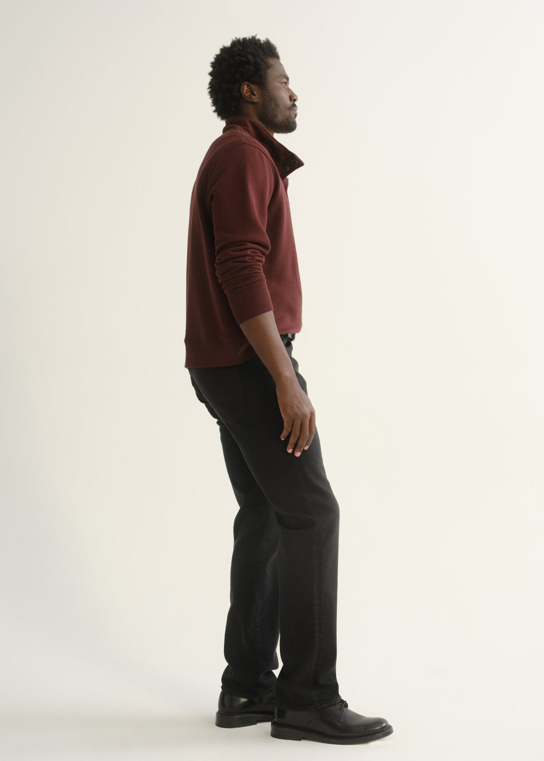 Person wearing burgundy half-button pullover with black pants and black shoes, angled front view