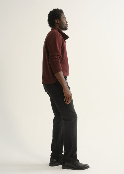 Person wearing burgundy half-button pullover with black pants and black shoes, angled front view