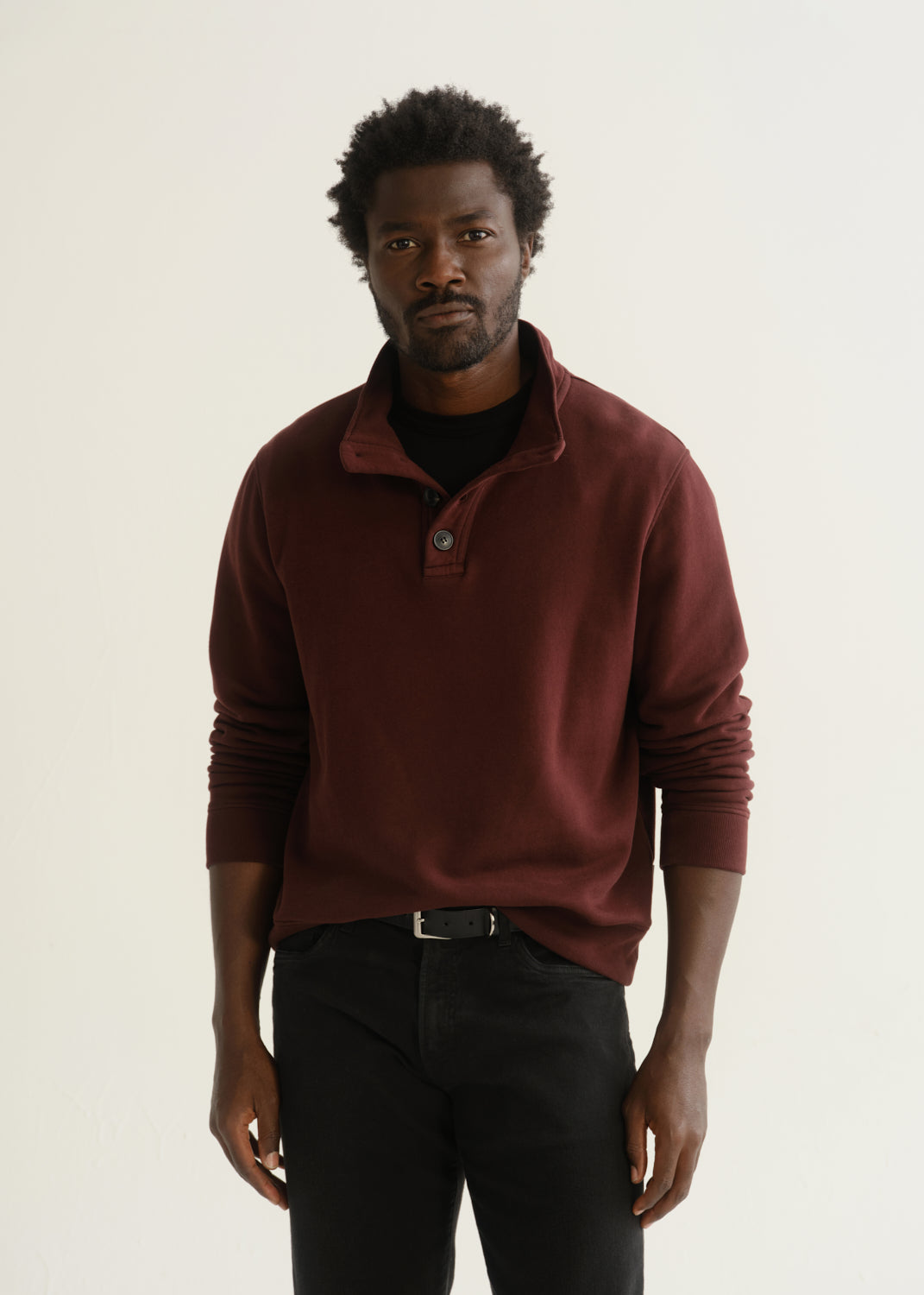 Person wearing burgundy half-button pullover with black pants and black shoes, front crop view