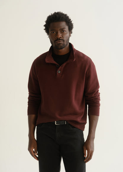 Person wearing burgundy half-button pullover with black pants and black shoes, front crop view