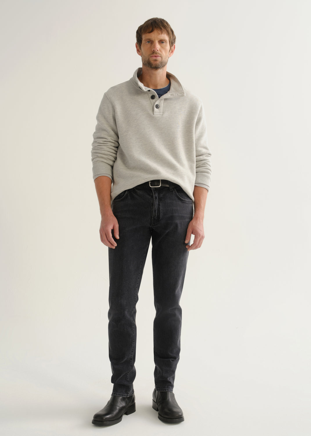 Person wearing a light grey long sleeve polo pullover, black jeans, and black boots, front full body view on a light grey background.