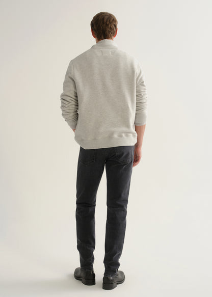 Person wearing a light grey long sleeve polo pullover, black jeans, and black boots, back full body view on a light grey background.