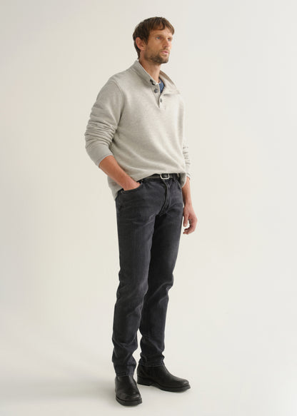 Person wearing a light grey long sleeve polo pullover, black jeans, and black boots, angled front full body view on a light grey background.