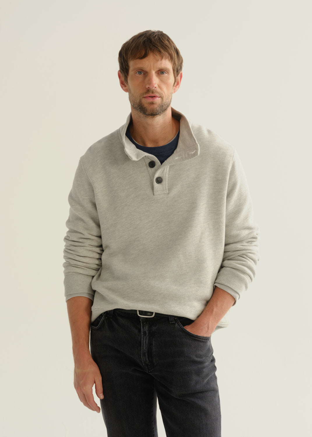 Person wearing a light grey long sleeve polo pullover and black jeans, front cropped view on a light grey background.