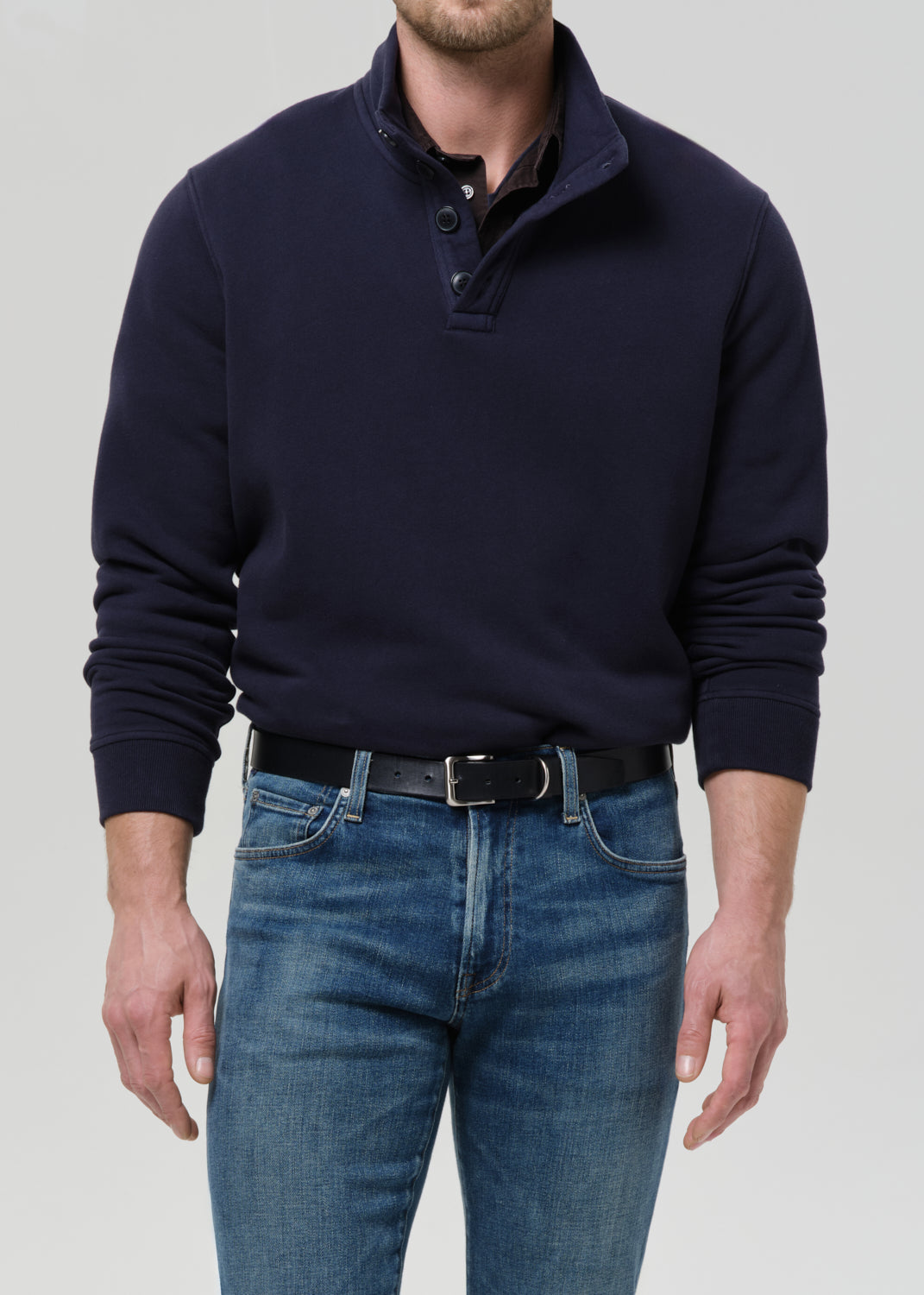 Person wearing a navy sweater and blue jeans on a grey background