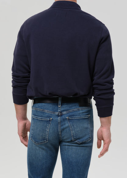 Person wearing a navy jacket and blue jeans on a grey background