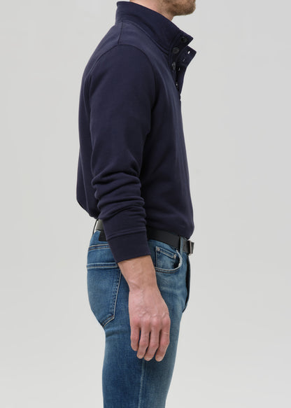 Man wearing a navy jacket and blue jeans on a grey background