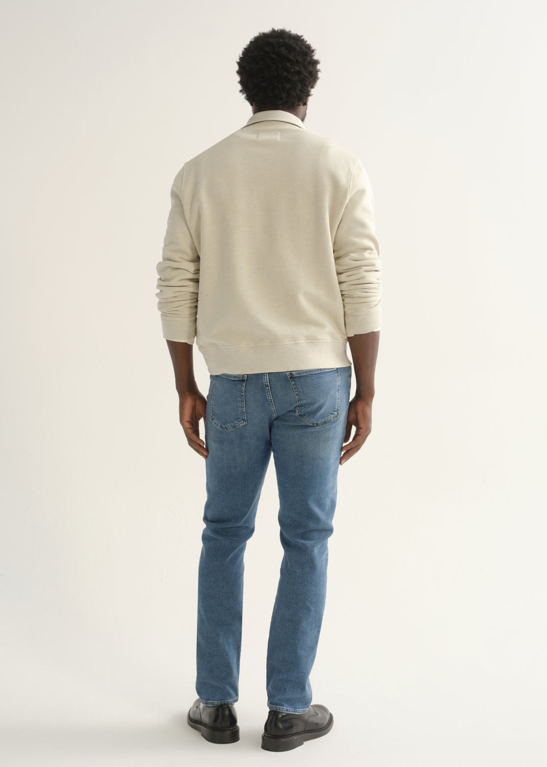 Person wearing cream rugby pullover and blue jeans front three-quarter view