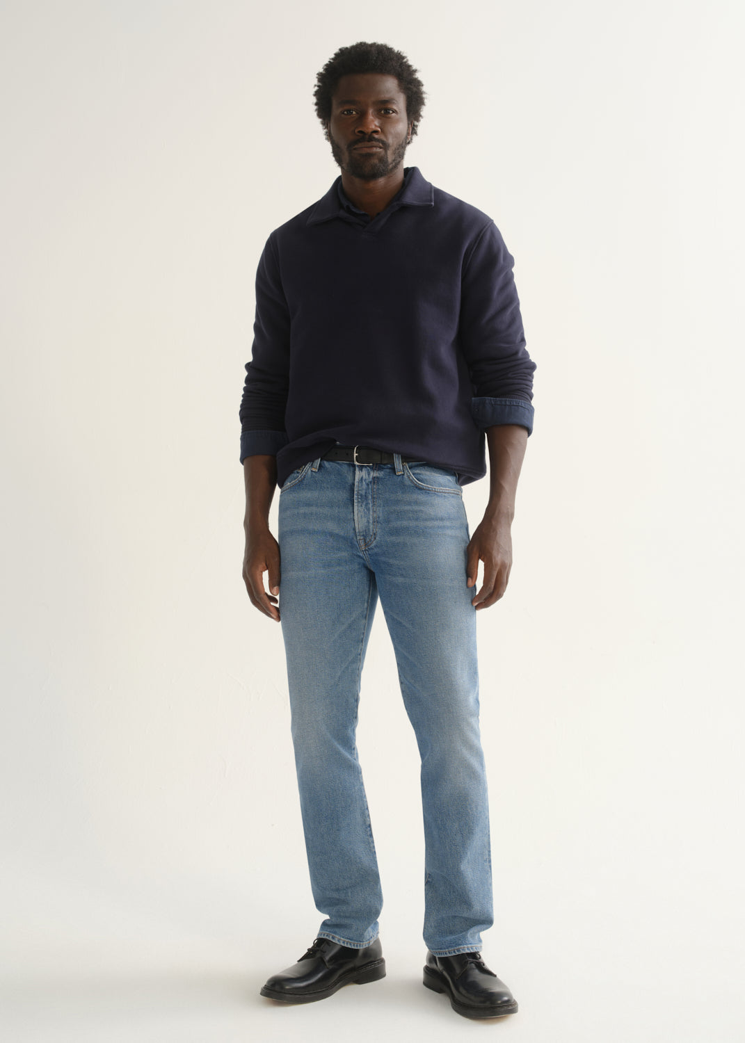 Person wearing a navy blue long sleeve pullover with light blue jeans and black shoes, front full body view on a light grey background.