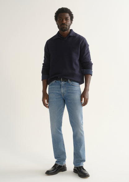 Person wearing a navy blue long sleeve pullover with light blue jeans and black shoes, front full body view on a light grey background.