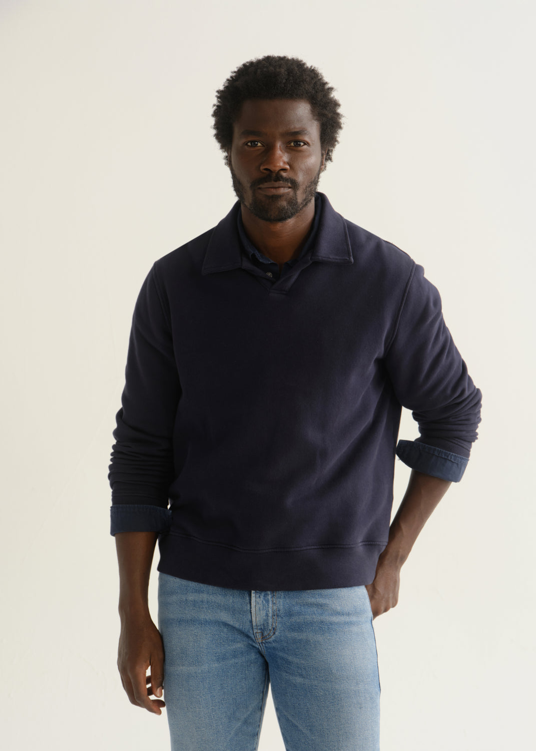 Person wearing a navy blue long sleeve pullover with light blue jeans, front cropped view on a light grey background.
