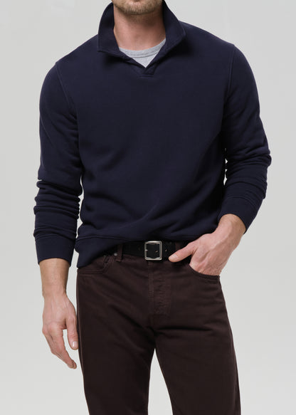 Man wearing a navy sweater and dark pants on a grey background