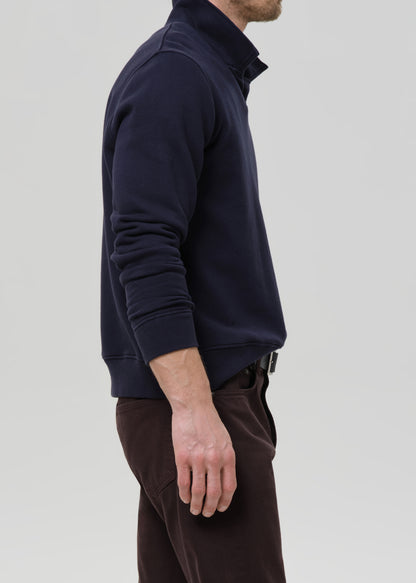 Person wearing a navy blue pullover with a zipper on a grey background