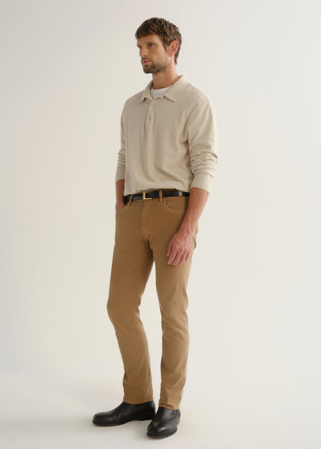 Person wearing a cream long sleeve polo pullover, tan pants, and black boots, angled front full body view on a light grey background.