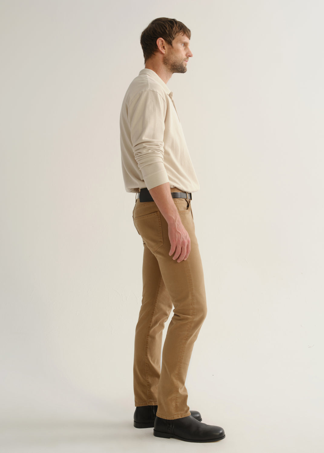 Person wearing a cream long sleeve polo pullover, tan pants, and black boots, side full body view on a light grey background.