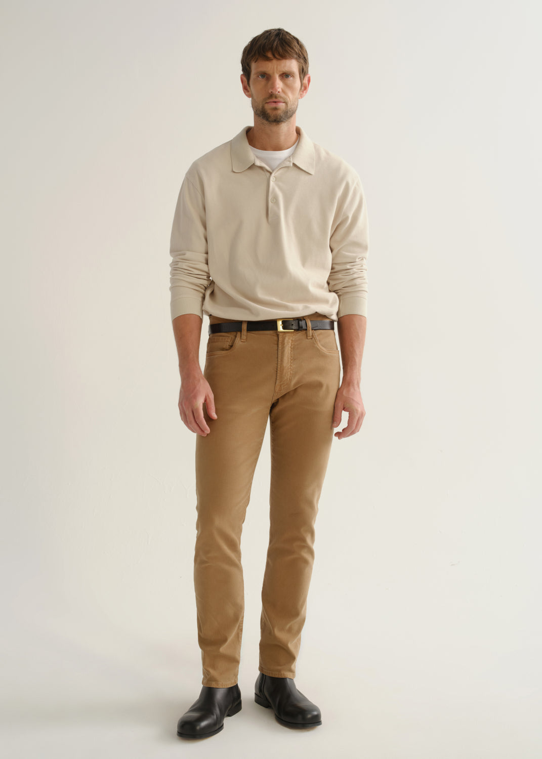 Person wearing a cream long sleeve polo pullover, tan pants, and black boots, front full body view on a light grey background.