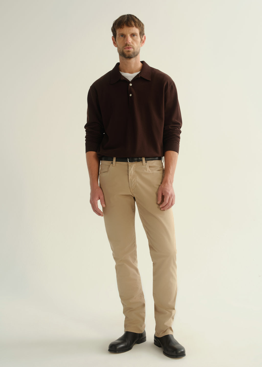 Person wearing a dark brown long sleeve polo pullover, beige pants, and black boots, front full body view on a light grey background.
