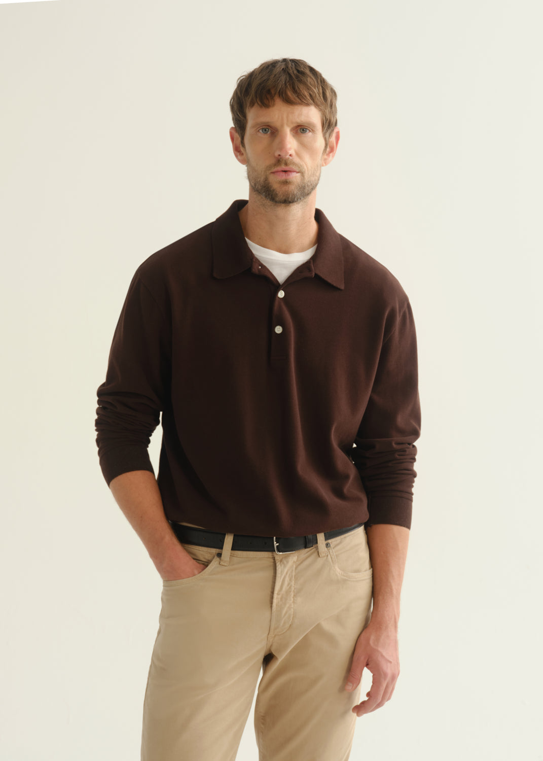 Person wearing a dark brown long sleeve polo pullover and beige pants, front cropped view on a light grey background.