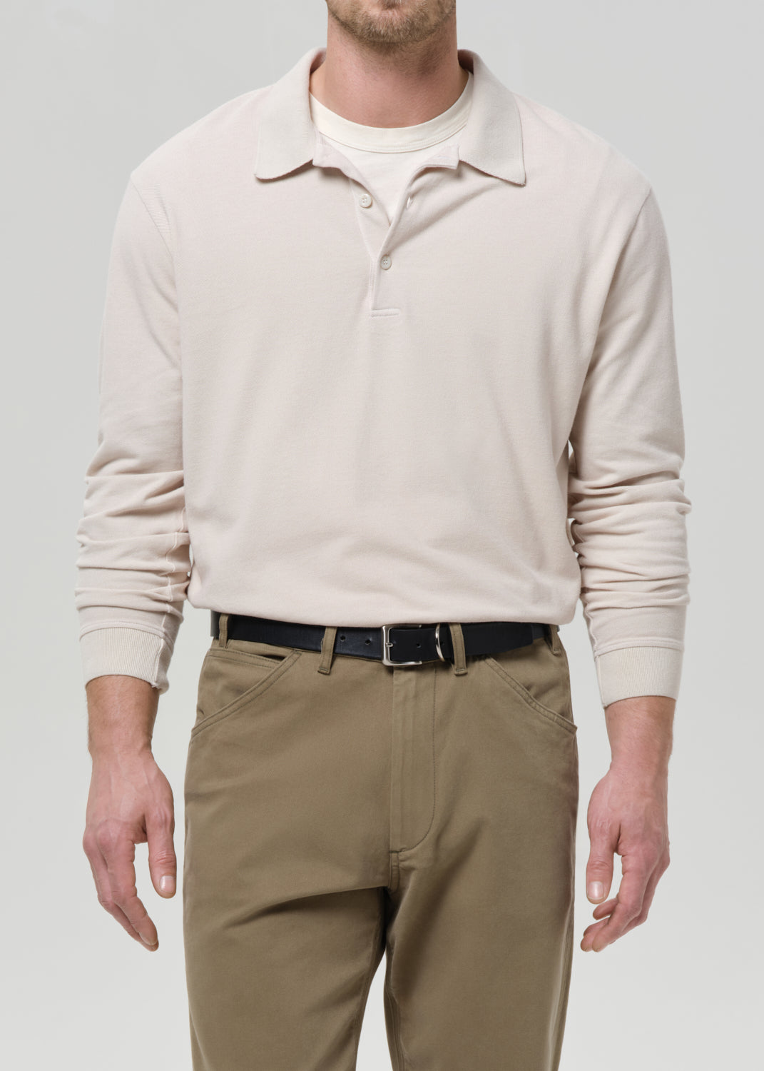 Man wearing a beige long-sleeve polo sweater and khaki pants on a grey background