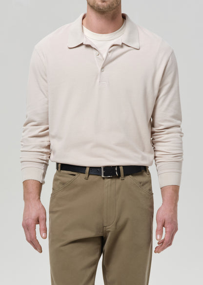 Man wearing a beige long-sleeve polo sweater and khaki pants on a grey background
