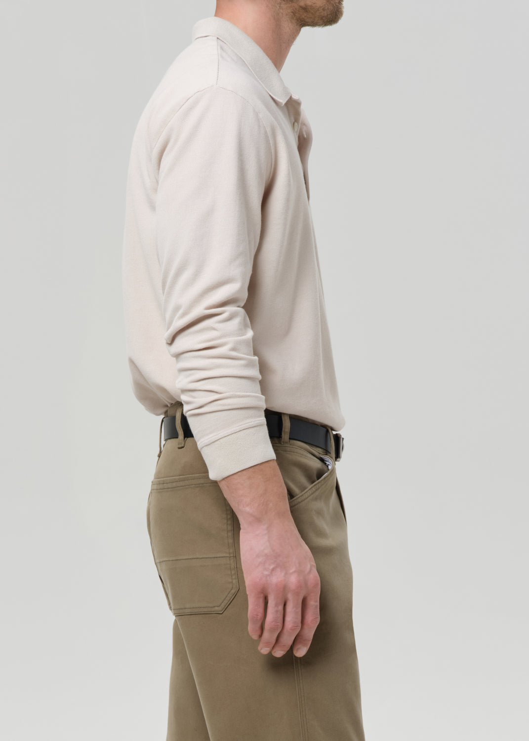 Person wearing a beige polo sweater and khaki pants on a grey background