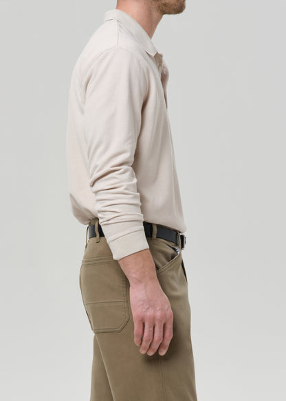 Person wearing a beige polo sweater and khaki pants on a grey background
