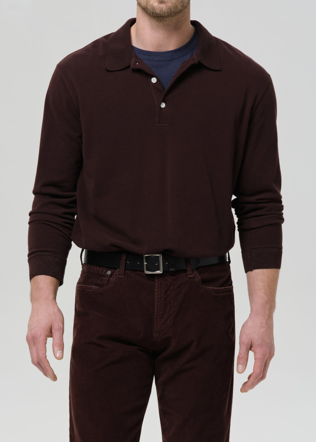 Man wearing a brown long-sleeve polo shirt and dark pants on a grey background