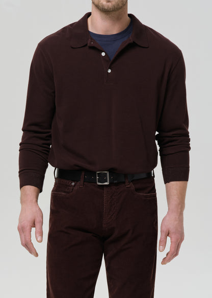Man wearing a brown long-sleeve polo shirt and dark pants on a grey background