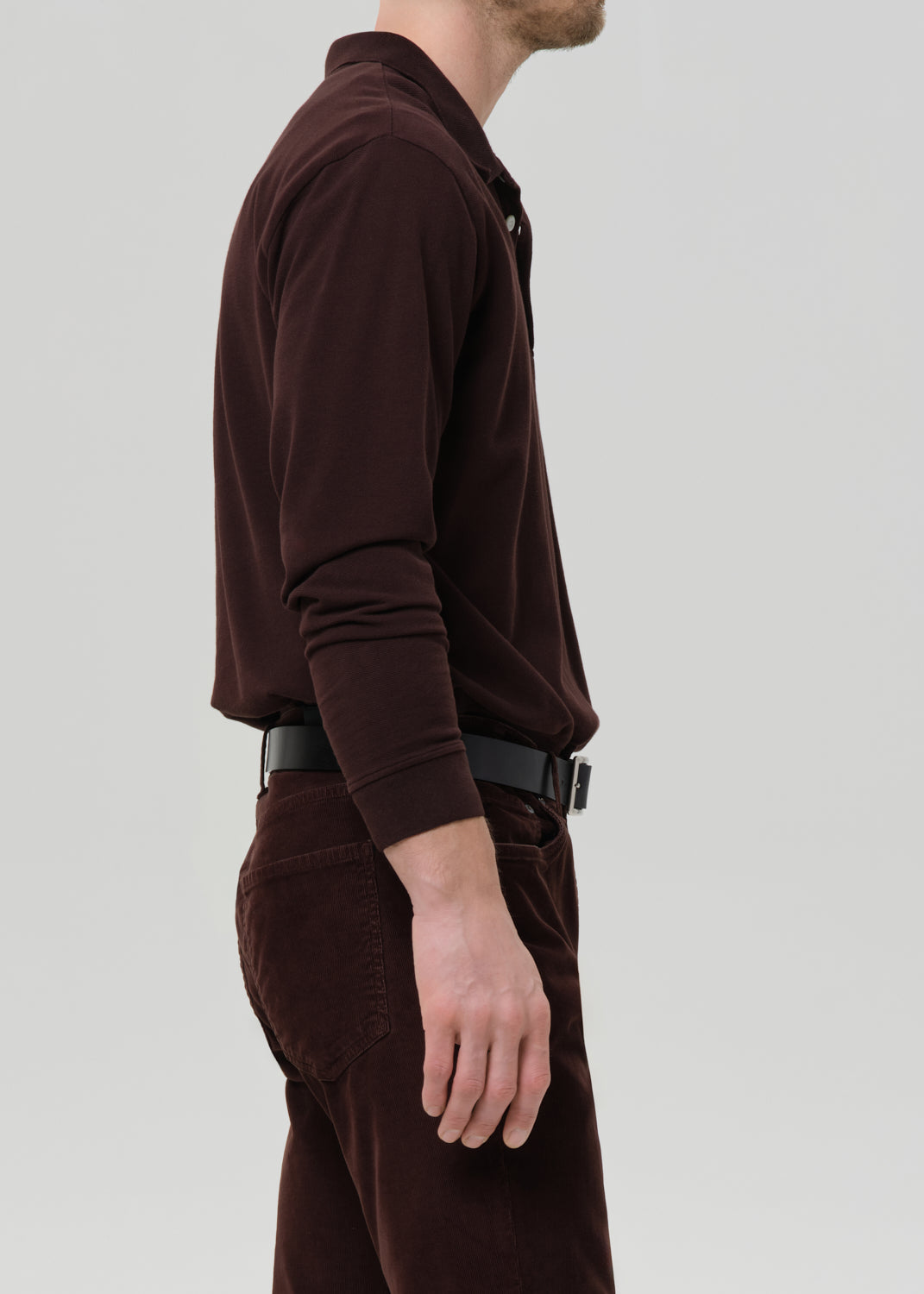Person wearing a brown long-sleeve polo shirt and pants on a grey background