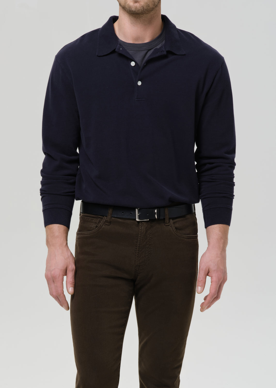 Person wearing a navy long-sleeve polo shirt and brown pants on a grey background.