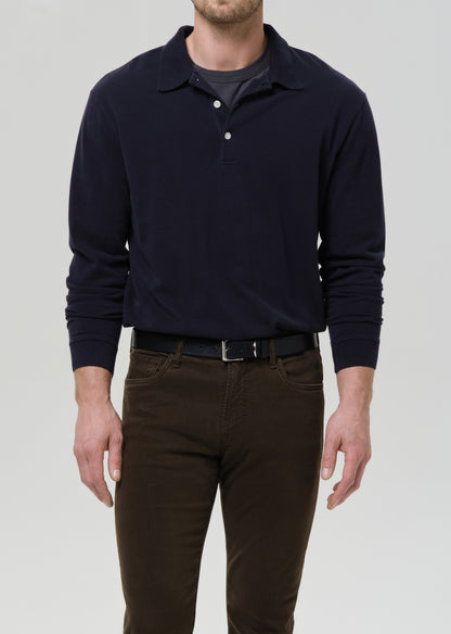 Person wearing a navy long-sleeve polo shirt and brown pants on a grey background.