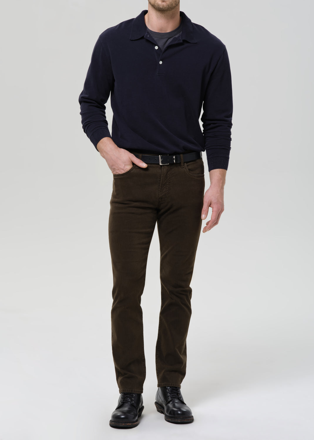 Man wearing a navy sweater and brown pants on a grey background.