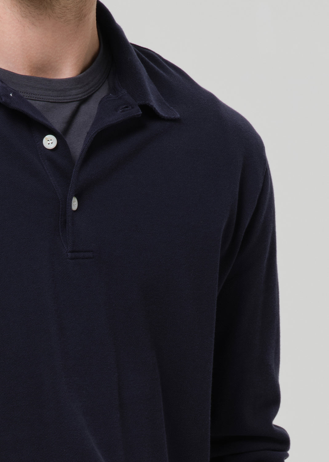 Navy long-sleeve polo shirt with button details on a grey background.