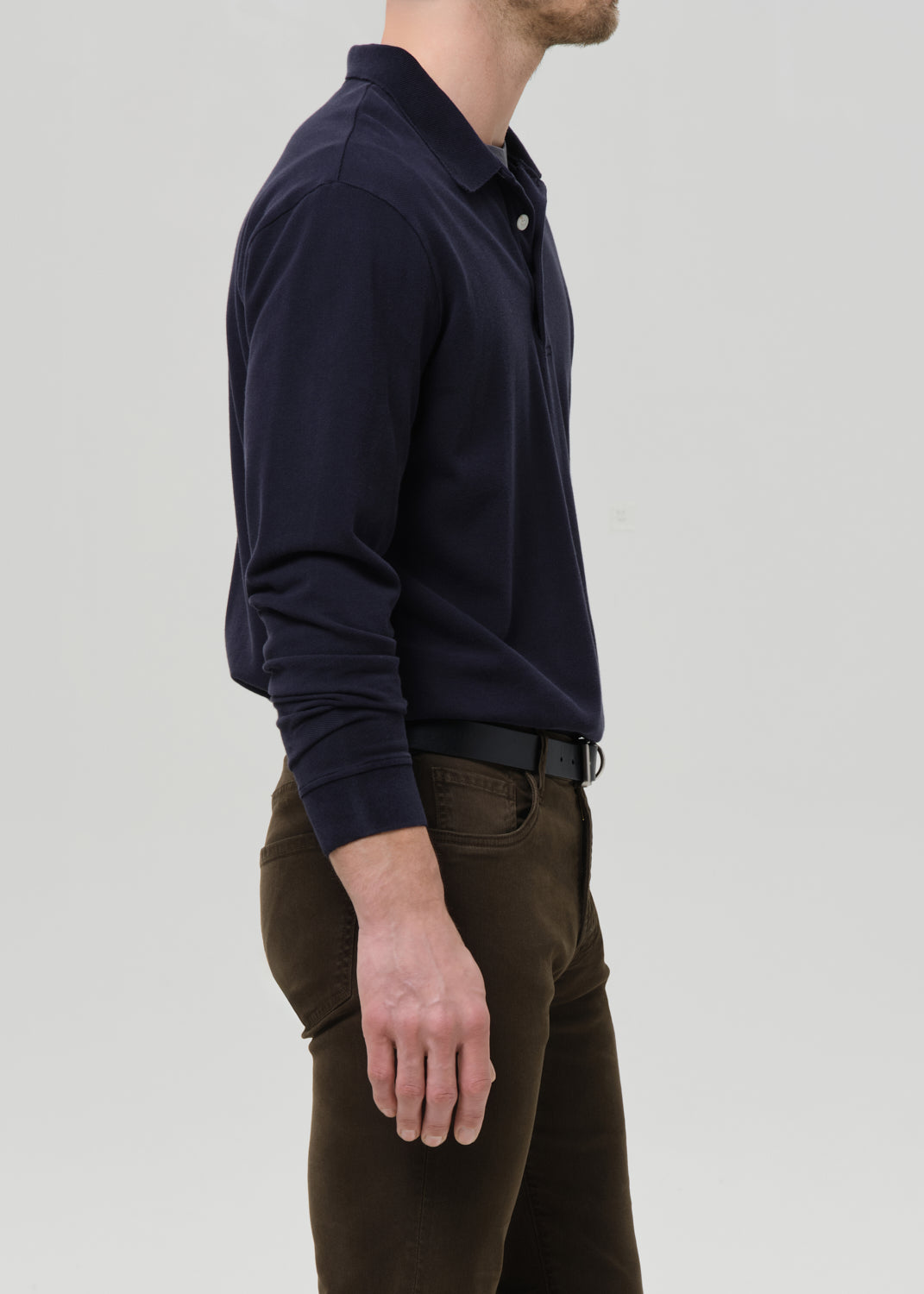 Man wearing a navy long-sleeve shirt and brown pants on a grey background.