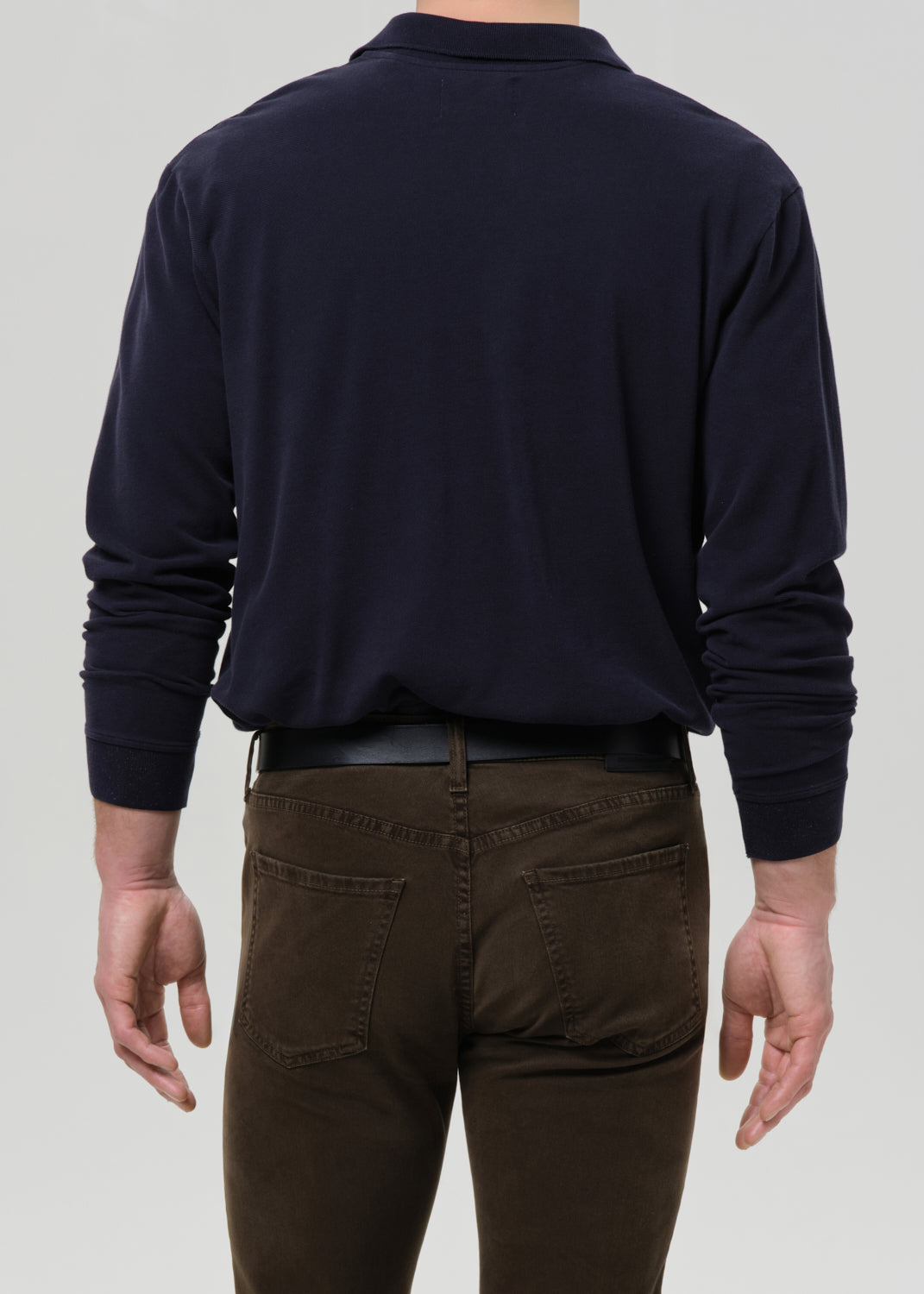 Person wearing a navy long-sleeve shirt and brown pants on a grey background.