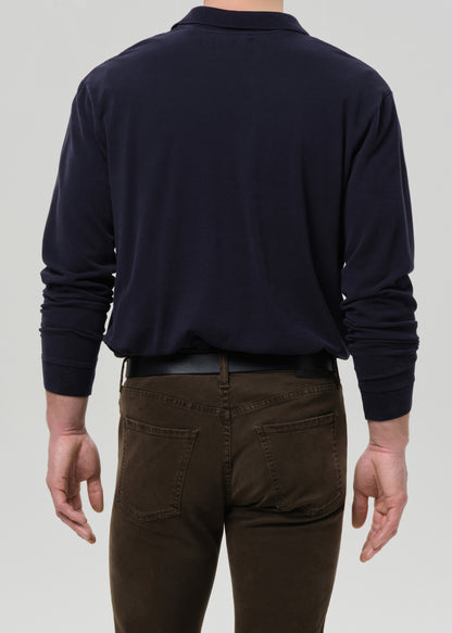 Person wearing a navy long-sleeve shirt and brown pants on a grey background.