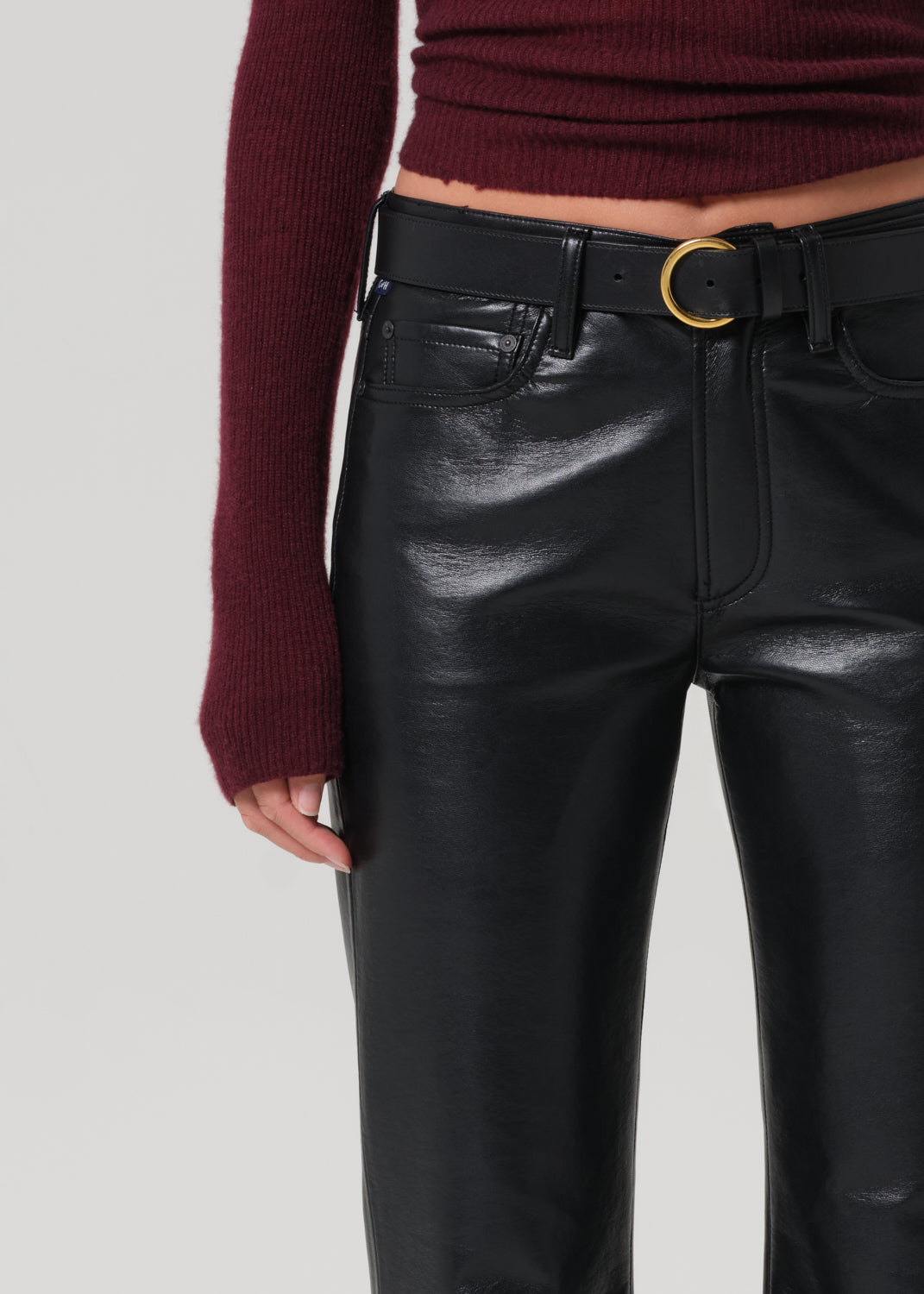 Person wearing black leather pants with a gold belt on a light gray background