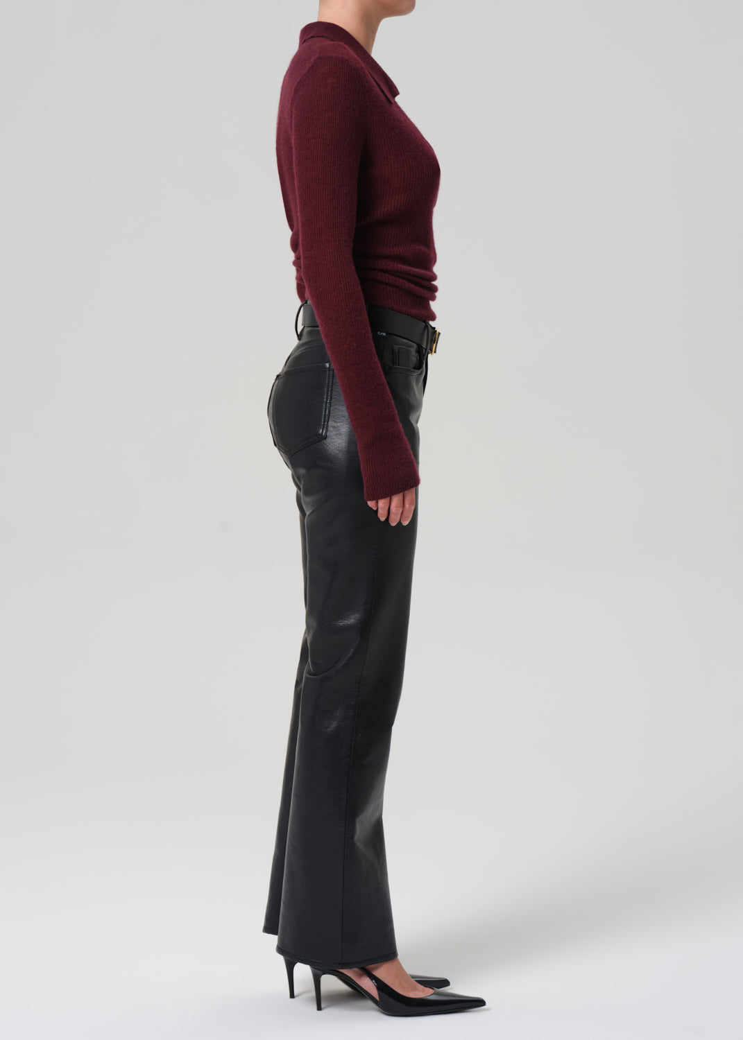 Person wearing a burgundy sweater and black leather pants on a white background